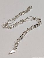 Full length view of polished silver chain bracelet laid out showing chain links and clasp.