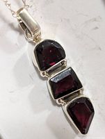Close-up of garnet pendant stones in silver settings showing three faceted garnet stones in unique shapes on a silver chain.