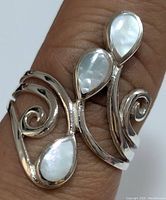 Close-up image of silver ring displaying three pear-shaped mother of pearl inlays set vertically with surrounding swirl design on the band. Ring shown worn on finger.