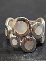 Front close-up of silver ring showing multiple mother of pearl inlays in circular and oval shapes.