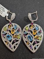 Front view of the pair of silver multi gemstone earrings showing the leaf shape and various colorful gemstones.