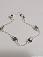 Full view of the silver chain necklace with multiple colored gemstones like green, red, black, and smoky brown on a white background.