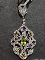 Front view of the silver pendant showing the pear-shaped blue topaz on top and intricate gemstone arrangement