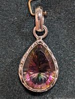 Close-up front view of silver pendant with pear-shaped mystic topaz gemstone showing faceting and iridescence on dark background.