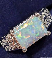 Close-up front view of silver ring's rectangular opal and filigree band detail