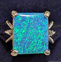 Close-up top view of a square opalite stone set in silver ring with visible prongs and sparkling blue-green tones.