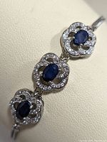 Close-up of three linked floral-shaped components with blue sapphire stones and cubic zirconia petals on silver bracelet.