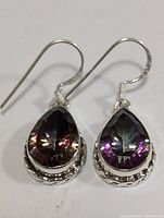 Close up front view showing the faceted multicolor sapphire teardrop stones set in silver with braided rope detail and hook ear wires.