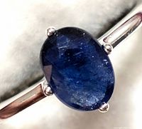 Close-up of the oval blue sapphire stone in the silver ring showing the deep blue color and facets.