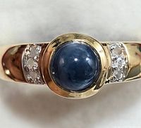 Close-up photo showing front view of silver ring with central blue tanzanite cabochon stone and diamonds on the sides.