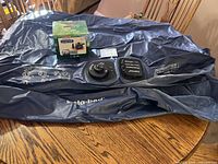 Overview of deflated blue Insta-bed air mattress and boxed Coleman QuickPump on wooden surface