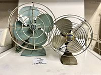 Front view of both vintage fans showing blades, cages, size comparison
