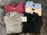 Stack of five folded sweaters showing colors and brands