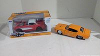 Photo showing two diecast muscle cars: boxed 1957 Chevy Corvette in red and white, and a loose orange muscle car.