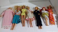 Seven Barbie dolls laid out side by side showing varying clothing and hair styles.