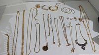 Full lot of all 20 pieces laid out on white surface. Includes necklaces, bracelets, hoop earrings, stud earrings, and pendants all in gold tone with some wear and tarnish.