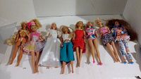 Eight Barbie dolls laid out showing different outfits and styles.