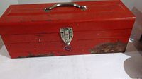 Red metal toolbox closed showing exterior rust and paint wear