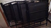 Four black metal and mesh folding chairs stacked unfolded backs facing out.
