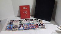 Loose sports trading cards, black card binder, and red baseball card booklet arranged on table.