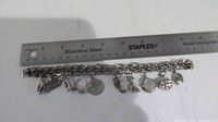 Photo of 8-inch silver charm bracelet with ruler for size reference, showing all 10 charms attached, some tarnish visible.
