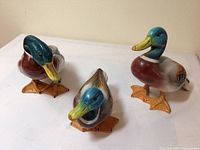 Three ceramic duck figurines arranged on a flat surface showing front and side views, highlighting varied sizes and multicolored shiny glaze