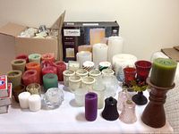 Long view showing a variety of wax candles, battery flameless candles in packaging, and assorted candle holders made of glass, ceramic, and wood.