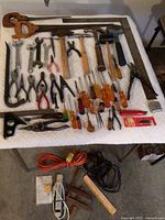 Wide view of assortment of hand tools laid out on a quilted surface including saws, hammers, pliers, screwdrivers, and extension cords.