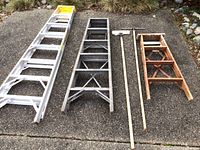 View of all three ladders laid out on the ground along with three long-handled cleaning tools, showing relative size and condition.