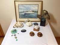Full lot arranged on a white tablecloth against wall featuring framed watercolor, seashell, coral pieces, jewelry, painted stones, decorative boxes, and fish sculpture.