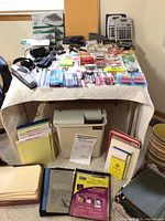 View of entire table showing a wide variety of office supplies like hole punches, tape, staplers, pens, folders, calculators, notebooks and a paper shredder underneath the table.