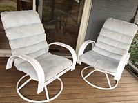 Two white metal patio chairs with padded cushions, positioned on wooden deck. Chairs have circular base for rocking and spinning.