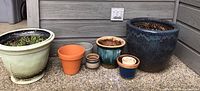 Photo showing entire set of 8 planters of various sizes and colors arranged on patio.