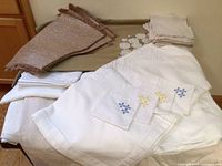 Photo showing large white linens with embroidery, beige linens, and a brown textured stack