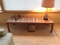 Overall view of long rectangular tile top table with items on top including MCM ceramic lamp, two carved wooden gazelles, and the metal waste basket underneath.