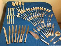 Overview of complete flatware set laid out on blue cloth