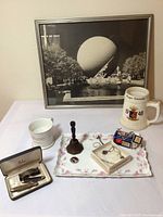 Overview of all items in the lot including framed 1939 World's Fair print, shaving mug, spectacles, pocket knives, bell, and small decorative tray with jewelry and other small pieces.