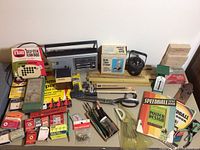 Full overview of vintage office supplies including radio, rulers, pens, books, and staplers laid out on a table.