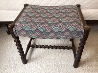 Front view of bench showing upholstered patterned seat and turned legs.