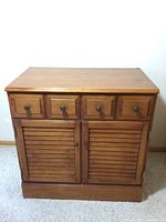 Front view of Sterling House wooden cabinet with four knobs on one drawer and two louvered doors.