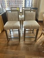 Four light fabric upholstered counter stools with metal frames, arranged in two rows of two against a window. Seats about 26 inches high.