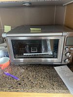 Front view of a stainless steel Breville toaster oven on a kitchen counter with control buttons and display on the right and the Breville logo on front.