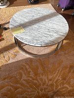 Full view of the circular stone coffee/side table showing white and gray marble top and metal circular base on a carpet.