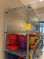 Metal wire shelving unit with six shelves, some shelves holding colorful plastic pots (not included with sale). Shelf unit is tall, chrome finish, with grid-style metal shelves and rimmed edges.