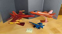 Photo showing all three fighter jet models: two mahogany jets and one blue and yellow metal F/A-18 Hornet.