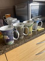 Four McIntosh Claude Monet series mugs featuring detailed landscape artwork, arranged on kitchen counter with toaster in background.