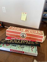 Stack of three items showing Marine Models kit box on top, Monopoly Classic game box below, and Dragon Kite package.