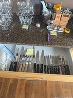 Countertop with glassware and kitchen items above an open drawer showing knives organized with various handles and blade types.