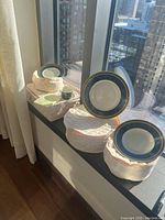 Photo showing several plates and bowls in protective cloth cases, set displayed on window ledge with city view.