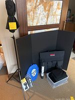 Photo of Sunpak Ebox light on tripod, Lastolite reflector case, backdrops, spray can, and storage box with black fabric